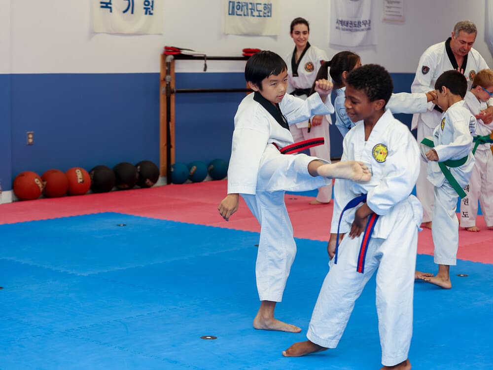 an asian boy and a black boy in taekwondo uniform doing a friendly spar in Norristown PA